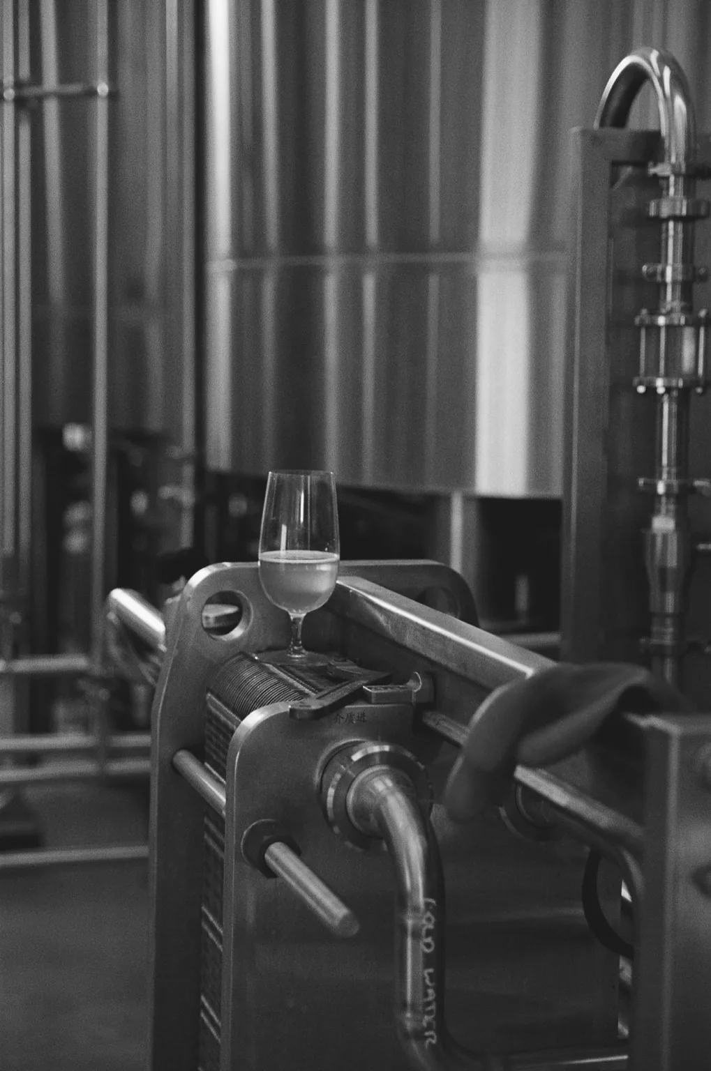 A glass of product resting beside stainless-steel processing equipment